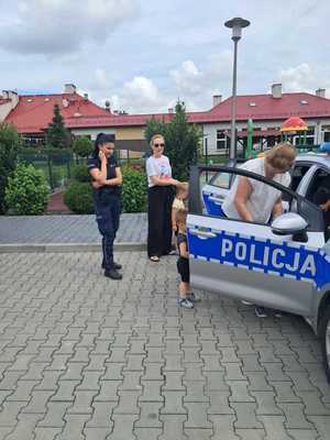 Policjantka oraz opiekunka z dziećmi przy radiowozie policyjnym