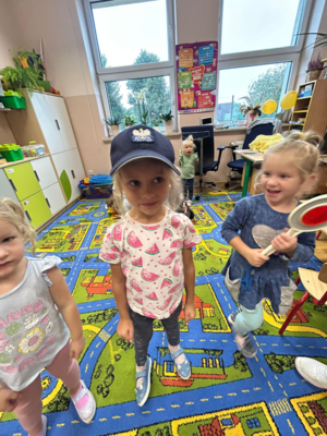 Dziewczynka w czapce policyjnej, obok trzymająca w ręce tarczę do kierowania ruchem