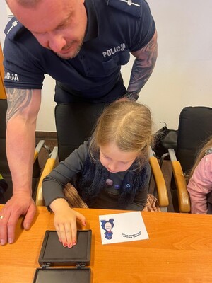 Policjant pokazuje przedszkolakowi jak wykonać odcisk palca