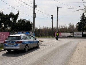 policjant stojący na skrzyżowaniu, za nim radiowóz policyjny