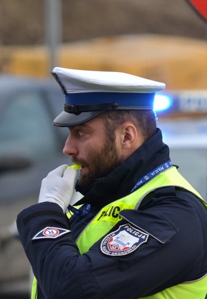 Policjant ruchu drogowego trzyma w ręku gwizdek podejmując ręczną regulację ruchem na drodze.