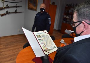 Prezes Spółdzielni trzyma w ręku dyplom. W tle Komendant Powiatowy Policji w Wieliczce